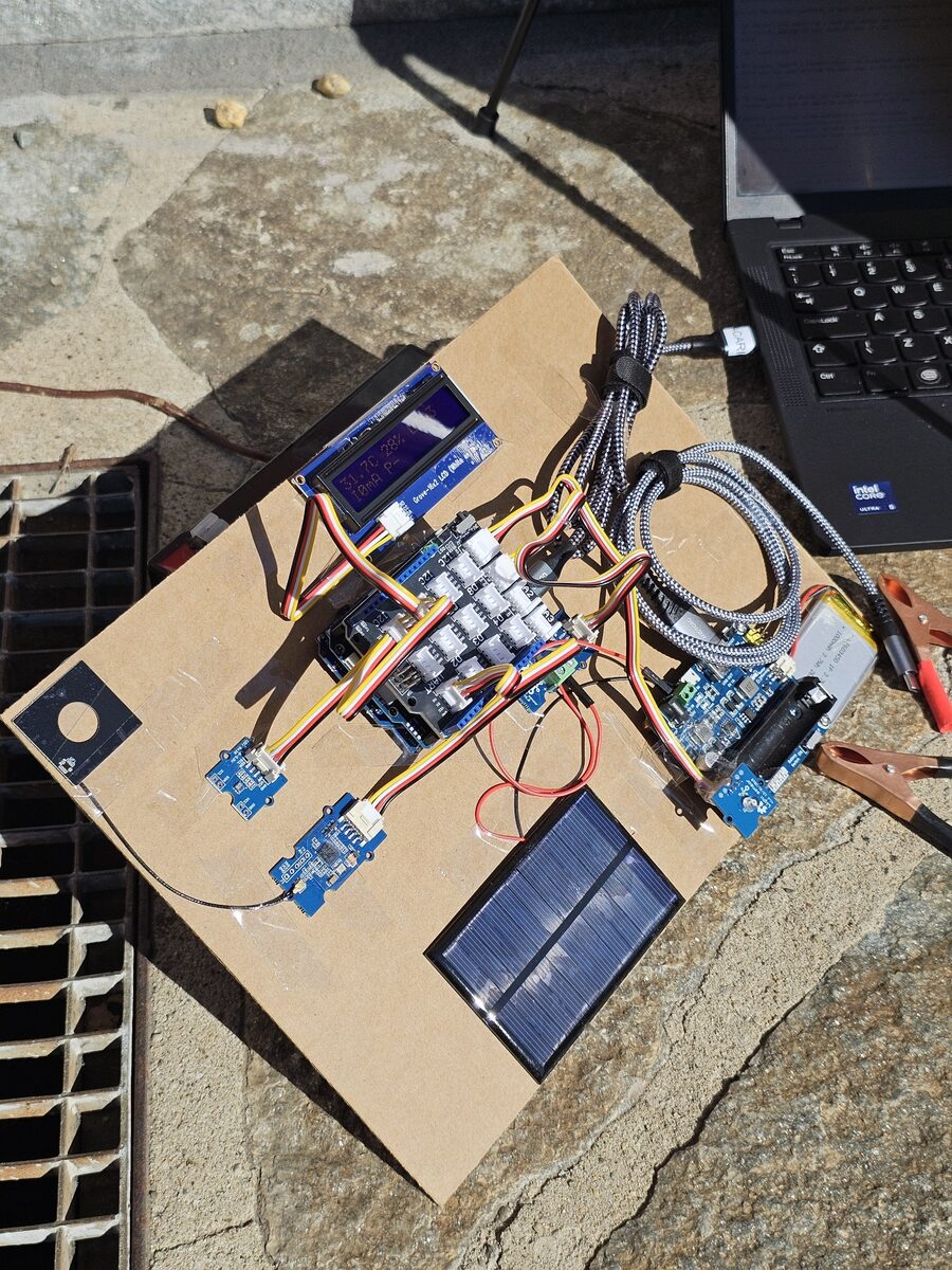 PoopVolt prototype outdoors in the sun, next to a laptop, with the LCD showing live readings